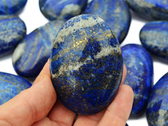 One blue and gold lapis lazuli palm stone crystal on hand with background with several stones