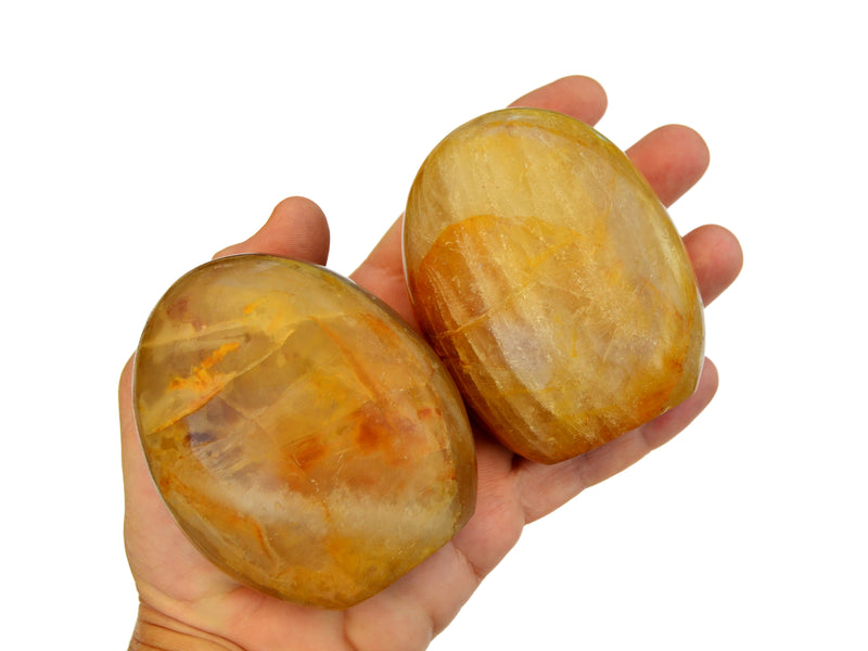 Two large yellow hematoid quartz free form stones on hand with white background