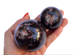Two rhodonite sphere stones 65mm-45mm on hand with white background