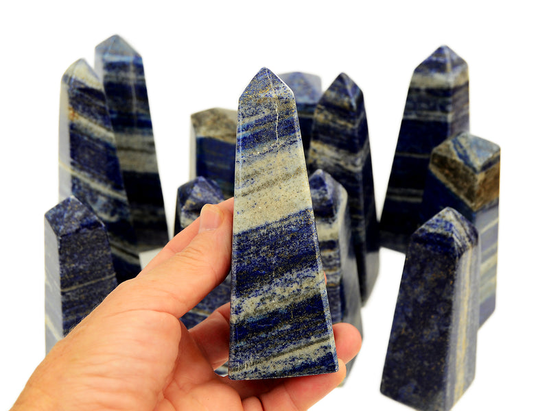 One lapislazuli obelisk 110mm on hand with background with some stones on white