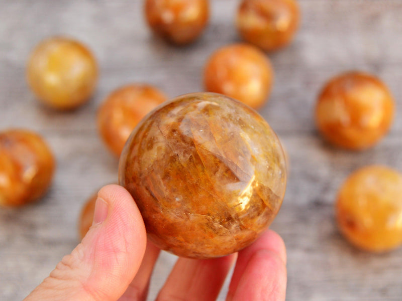 One golden healer quartz crystal sphere 50mm on hand with background with some hematoid balls on wood table