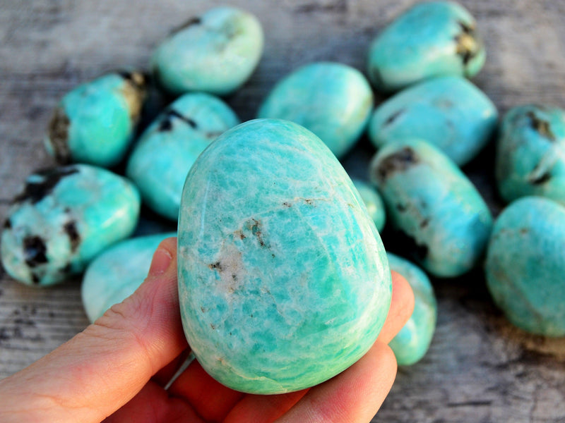 One chunky green amazonite tumbled on hand with background with some stones on wood table