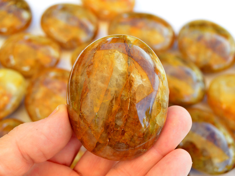 One golden healer quartz palm stone 60mm on hand with background with several crystals on white