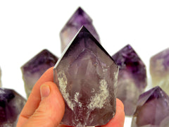 One amethyst semi polished point crystal 75mm on hand with background with some points on white