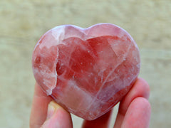 Rose calcite heart crystal 55mm on hand with wood background