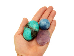 Amazonite palm stone, raw amethyst and blue calcite sphere on hand with white background