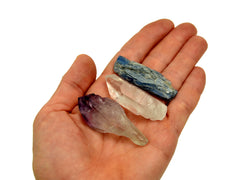 One raw amethyst point, clear quartz raw point and raw blue kyanite on hand with white background