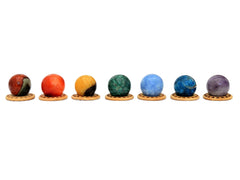 Mini spheres of polychrome jasper, carnelian, yellow septaria, chrysocolla, blue calcite, blue apatite and amethyst stones forming a horizontal line on wooden bases on a white background.