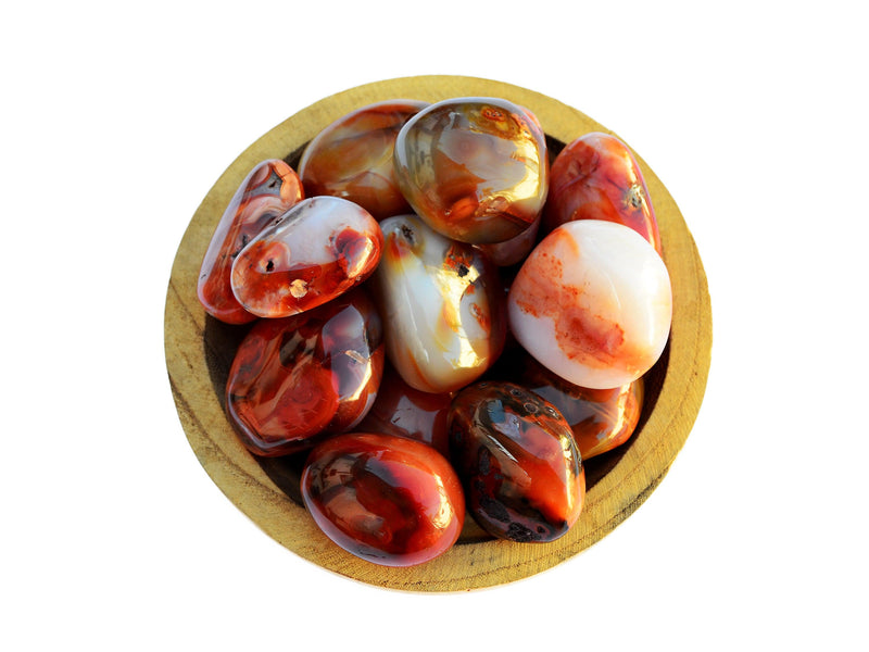 Several big carnelian tumbled minerals inside a wood bowl on white background