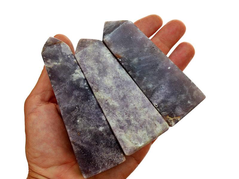 Three purple lepidolite crystal obelisks 95mm on hand with white background