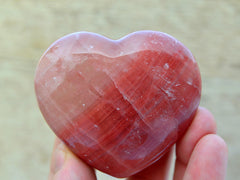 Rose calcite heart crystal 70mm on hand with wood background