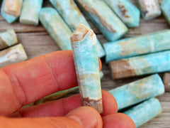 One blue aragonite point crystal 50mm on hand with background with several points on wood table