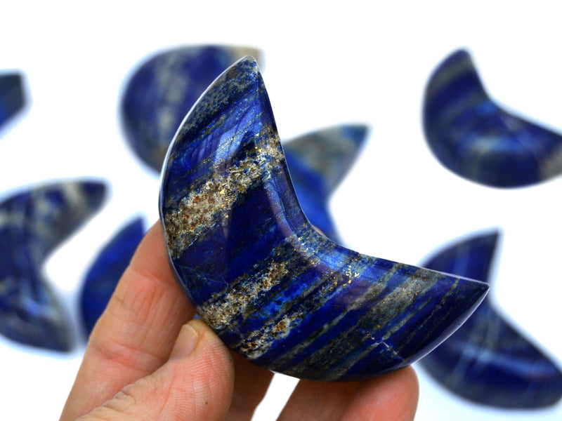 One lapis lapis lazuli mmon shaped crystal 70mm on hand with background with some stones on white