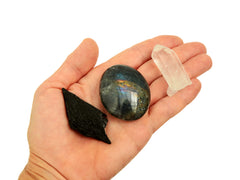 Small raw black kyanite, labradorite palm stone and raw clear quartz point on hand with white background