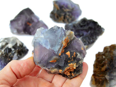 One rough purple fluorite stone on hand with background with some crystals on white