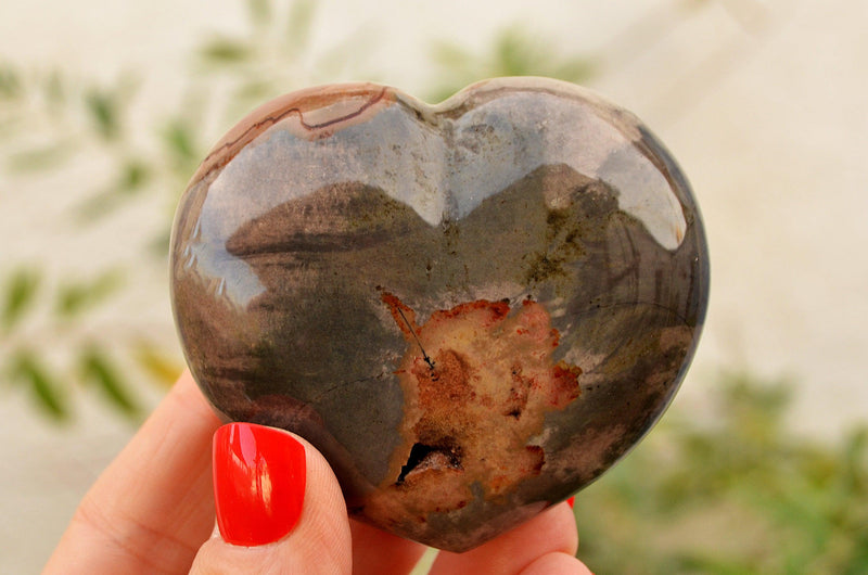 One large polychrome jasper  heart crystal 70mm on hand with background with green plants