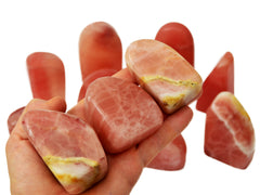 Three rose calcite free forms on hand with background with some stones on white