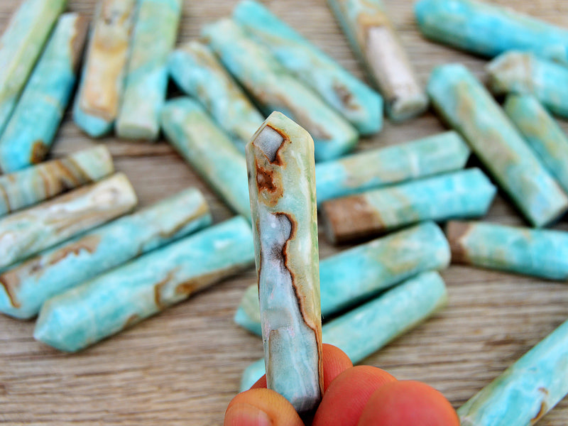 One blue aragonite point crystal 50mm on hand with background with several mini towers on wood table