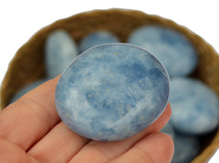 One blue calcite palm stone 40mm on hand with background with some stones inside a basket