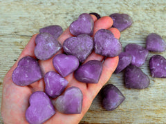Ten lepidolite crystal hearts 25mm-35mm on hand with background with some crystals on wood table