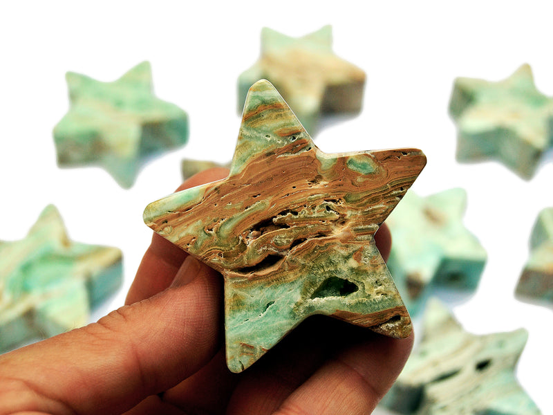 One blue aragonite stard shapped mineral on hand with background with some crystals on white