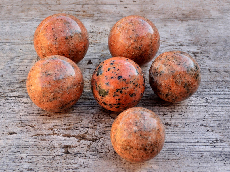 Six orange calcite sphere stones 65mm-95mm on wood table