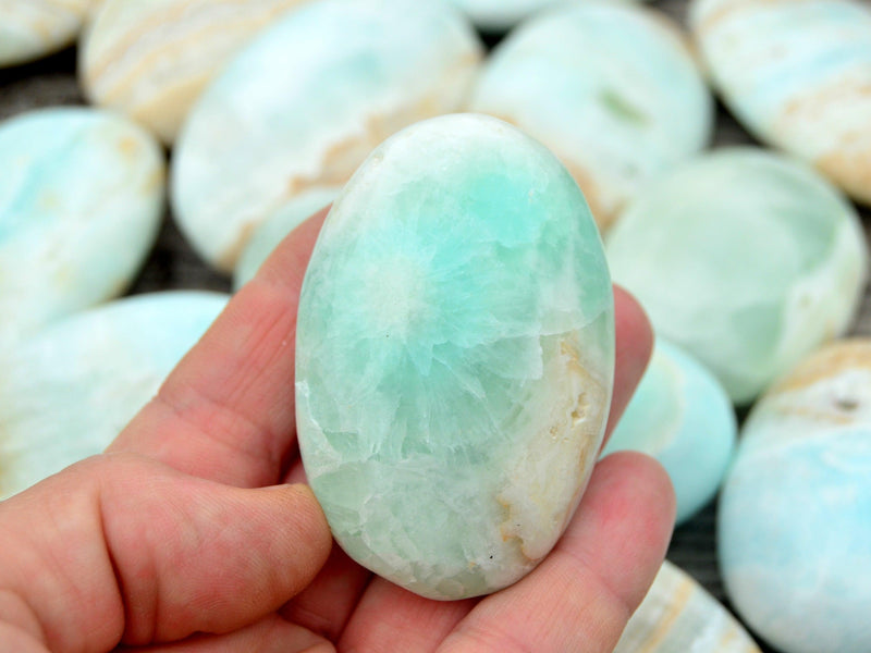 One blue caribbean calcite palm stone 45mm on hand with background with some crystals on wood table