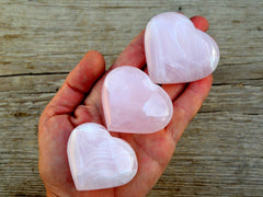 Three  lmangano calcite pink hearts 50mm-55mm on hand with wood background