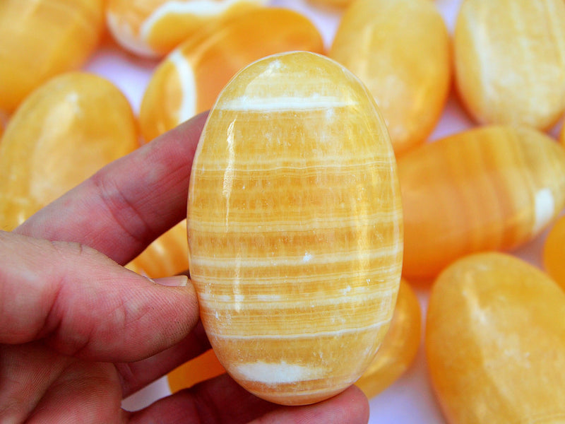 One banded orange calcite palm stone 70mm on hand with background with some crystals