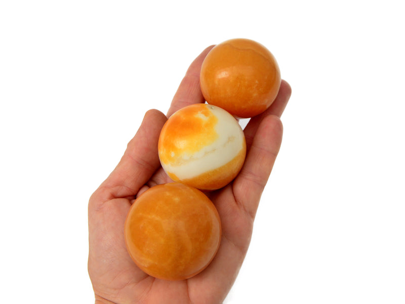 Three orange calcite mineral spheres 45mm on hand with white background