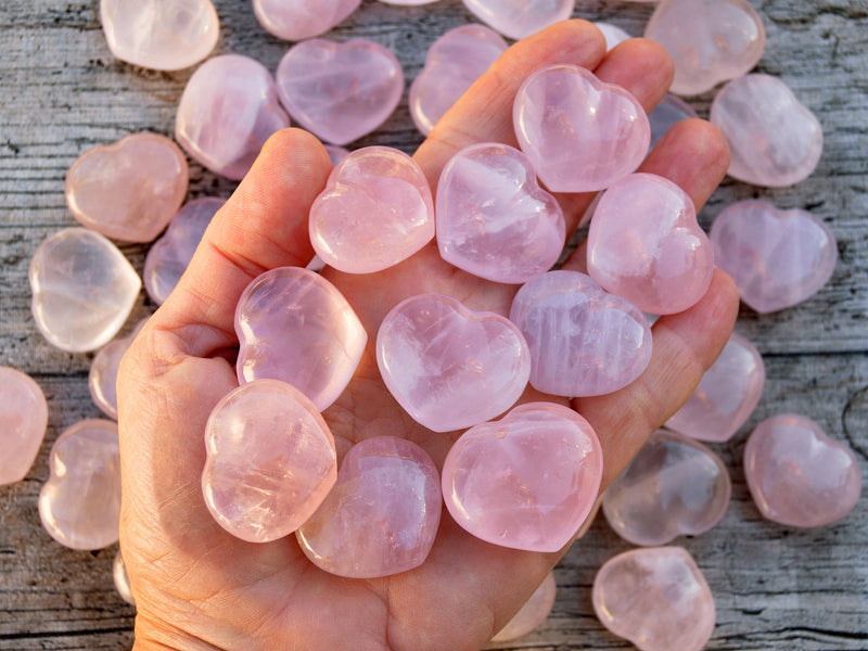 Ten rose quartz puffy heart crystals 30mm on hand with background with some heart stones on wood table