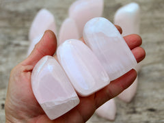 Three pink mangano free form stones 50mm-60mm on hand with background with some stones on wood table