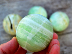 One green pistachio calcite sphere 60mm on hand with background with some balls on wood table