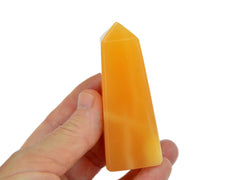 One orange calcite tower 80mm on hand with white background