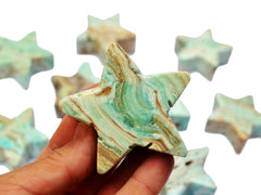 One blue aragonite stard carved crystal on hand with background with some stones on white