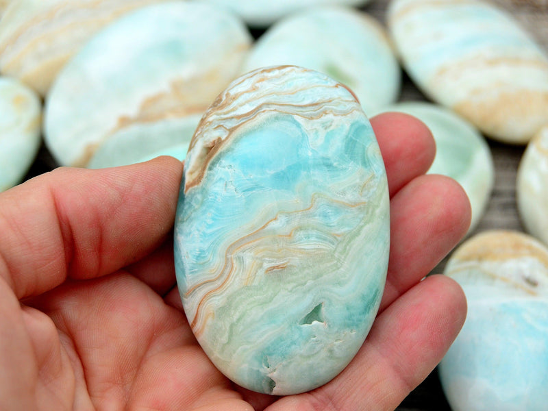 One blue caribbean calcite palm stone 50mm on hand with background with some crystals on wood table