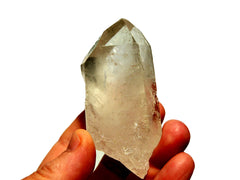 One raw clear quartz crystal point 80mm on hand with white background