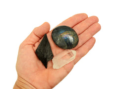 Labradorite palm stone, raw black kyanite and raw clear quartz point on hand with white background