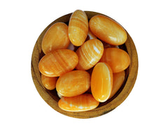 Several orange calcite palm stones inside a wood bowl on white background