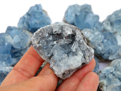 One mini raw celestite on hand with background with some crystals