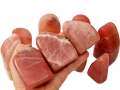 Three rose calcite free form stones 55mm on hand with background with some crystals