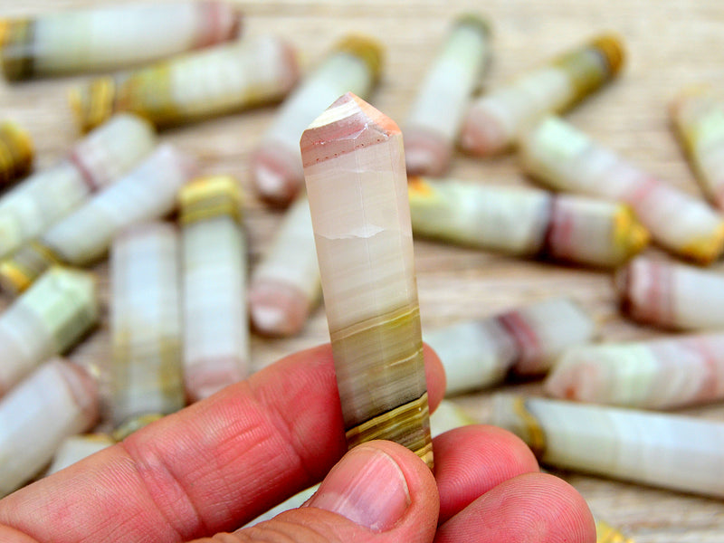 One pink banded onyx tower crystal 50mm on hand with background with several points on wood table