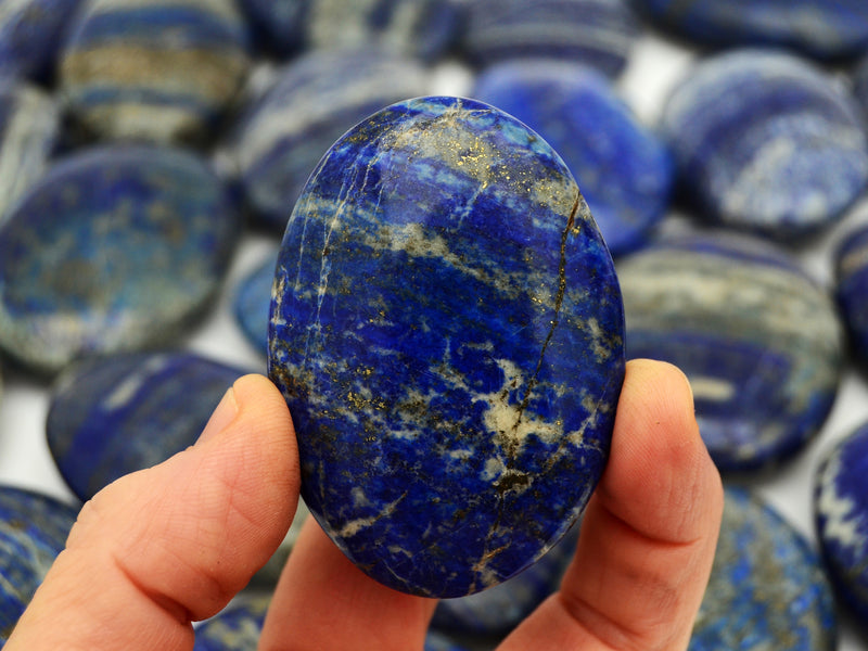 One lapis lazuli palm stone 70mm on hand with background with some lapis crystals on white 