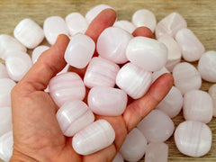 Some mangano calcite mineral tumbled stones on hand with background with some crystaks on wood table