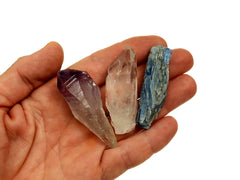 One raw amethyst crystal point, raw clear quartz point and raw blue kyanite on hand with white background