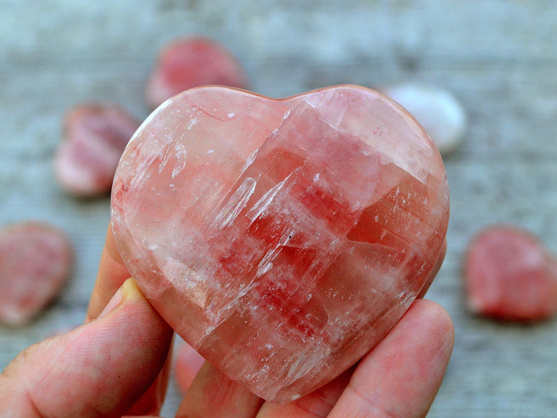 Rose calcite heart crystal 60mm on hand with wood background