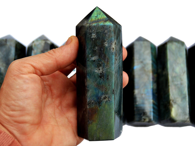 One large labradorite obelisk 110mm on hand with background with some points on white