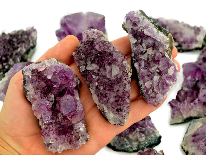 Three purple amethyst clusters 100mm on hand with background with some crystals on white