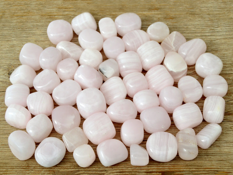 Several pink mangano calcite mini tumbled crystals on wood table