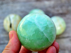 Green pistachio calcite sphere crystal 50mm on hand with background with some stones on wood table